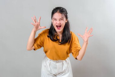 Genç Asyalı kadın öfkeyle bağırıyor ağzı açık ve elleri pençeli, yoğun bir hayal kırıklığı ya da öfke gösteriyor, duygusal ve dramatik reklam kavramları için anlamlı bir yüz..