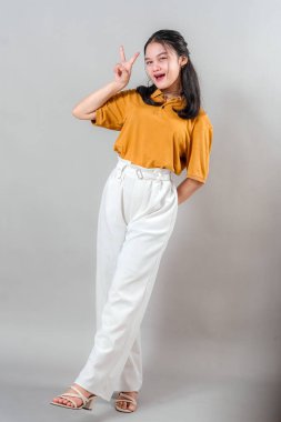 Neşeli, gülümseyen ve diş telleriyle sevimli bir barış işareti yapan Asyalı kadın. Neşeli ifadesi ve eğlenceli duruşu mutluluğu ve gençlik cazibesini yansıtıyor..