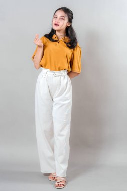 Neşeli, genç Asyalı bir kadının portresi güven içinde gülümserken parmaklarıyla kalp hareketi yaparak, dostça ve olumlu bir ifadeyle mutluluk ve cazibesini ifade ediyor..