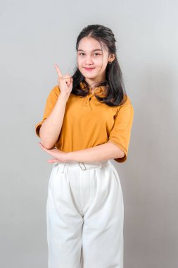 Genç Asyalı bir kadının portresi hafifçe gülümserken bir parmağıyla yukarı doğru işaret ederek bir fikir öne sürüyor. Onun sakin ve kendinden emin yüz ifadesi berraklık ve ilham veriyor..