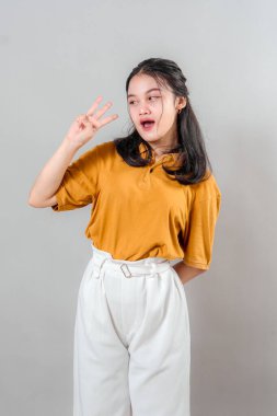 Kendinden emin gülümseyen neşeli, genç Asyalı kadın, rahat bir şekilde poz verirken üç parmak hareketi gösteriyor. Arkadaş canlısı, olumlu ve cana yakın bir görünüm..