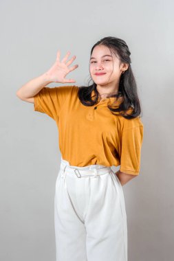 Çekici, Asyalı genç bir kadın güvenle gülümserken dostça bir selamla beş parmağını kaldırıyor. Onun anlamlı yüzü ve ışıl ışıl gülüşü sıcaklığı ve pozitif enerjiyi iletir..