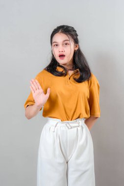 Asyalı genç bir kadının elini kaldırması sürpriz oldu. Sanki beklenmedik bir şeye dur ya da tepki ver der gibi. Reklam amaçlı kullanım için sade arka planda izole edilmiş.