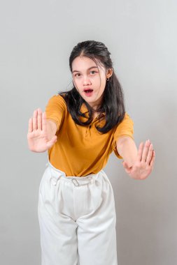 Şaşırmış ve dışavurumcu yüzü olan genç bir Asyalı kadın sanki dur der gibi iki elini de ileri doğru uzatıyordu. Ticari kullanım için gri arkaplanda izole.