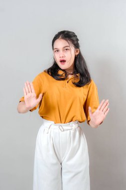 Şaşırmış ve dışavurumcu yüzü olan genç bir Asyalı kadın sanki dur der gibi iki elini de ileri doğru uzatıyordu. Ticari kullanım için gri arkaplanda izole.