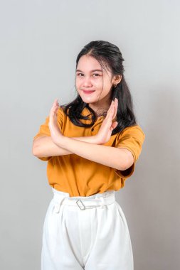 Hafif bir gülüşü olan genç Asyalı kadın göğsünün önünde çapraz kollar kullanarak hayır ya da hayır işareti yapıyor. Etkileyici yüz ve vücut dili, reklam kullanımı için mükemmel..