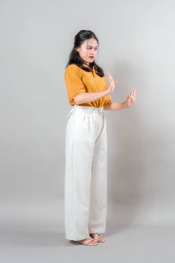 Asyalı kadın tiksinmiş ve rahatsız görünüyor, iki elini de reddederek reddediyor. Yüz ifadesi güçlü bir hoşnutsuzluk ya da hoşnutsuzluk gösteriyor..