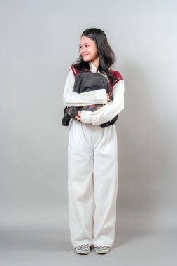 Genç kız yan bakarken hafifçe gülümsüyor, sırt çantasına sarılıyor. Onun nazik ifadesi sıcaklık, neşe ve doğal çekicilik taşır, pozitif ve genç reklamlar için idealdir..