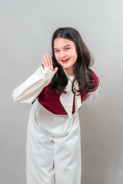 Çekici bir gülümsemesi ve arkadaş canlısı yüz ifadesi olan mutlu genç Asyalı kadın el sallıyor ve öne eğiliyor. Reklam, iletişim ve yaşam tarzı temaları için harika bir poz..