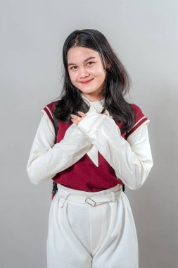 Sıcak bir gülümseme ve nazik bir ifadeyle genç bir kadın güven içinde ellerini göğsünün üstüne koyup samimiyetini, dostluğunu ve duygusal sıcaklığını ifade ediyor..