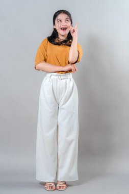 Şaşırmış ifadesi ve ağzı açık, sanki parlak bir fikre kapılmış gibi işaret eden heyecanlı genç bir kadın. Yaratıcı ve ilham verici temalar için mükemmel.