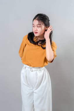 Gülümseyen genç bir kadın kulağını kavrıyor ve hafifçe öne eğiliyor, sanki dikkatle dinliyormuş gibi meraklı ve özenli bir ifade gösteriyor. İletişim temaları için harika.