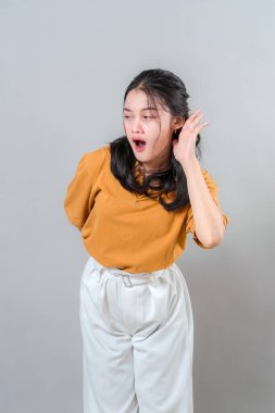 Gülümseyen genç bir kadın kulağını kavrıyor ve hafifçe öne eğiliyor, sanki dikkatle dinliyormuş gibi meraklı ve özenli bir ifade gösteriyor. İletişim temaları için harika.