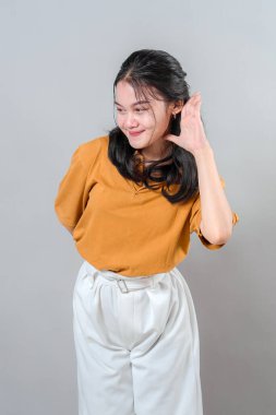 Gülümseyen genç bir kadın kulağını kavrıyor ve hafifçe öne eğiliyor, sanki dikkatle dinliyormuş gibi meraklı ve özenli bir ifade gösteriyor. İletişim temaları için harika.