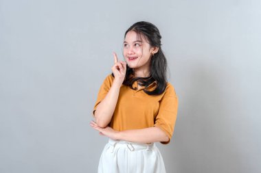 Neşeli bir yüz ifadesi olan genç bir kadın, bir parmağını aniden bir fikre kapılmış gibi kaldırıyor. Parlak gülüşü ve heyecanlı gözleri yaratıcı bir 