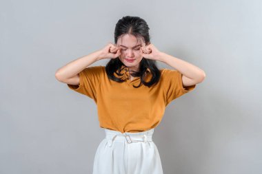 Üzüntüsünü ya da hayal kırıklığını ifade eden genç bir Asyalı kadın. Kapalı gözlerle ve yüzünü sıkan yumruklarla. Duygusal ve dramatik jest, ruh sağlığı temalarının reklamları için mükemmel..