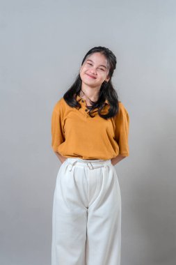 Neşeli bir yüz ifadesiyle gülümseyen mutlu, genç Asyalı kadın başını hafifçe eğiyor ve memnun görünüyor. Stüdyo portresi pozitifliği, dostluğu ve sıcaklığı gösteriyor..