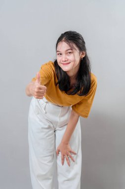 Genç Asyalı kadın başparmak işareti yaparken kendine güvenerek gülümsüyor. Onun neşeli ve onaylayıcı yüz ifadesi başarı ve pozitiflikle ilgili reklam temaları için idealdir..