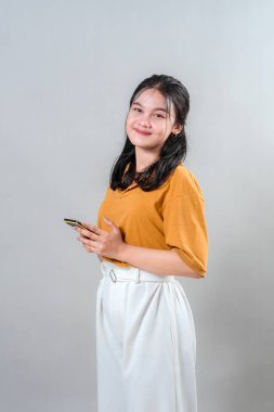 Akıllı telefonu tutarken sıcak ve kendine güvenen bir gülümsemesi olan Asyalı genç bir kadının portresi. Hoş yüz ifadesi, hayat tarzı, teknoloji ya da iletişim markaları reklamına uyuyor..