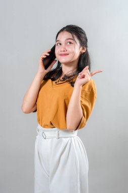 Genç Asyalı kadın telefonda konuşurken şaşırmış ve heyecanlı bir yüz ifadesi sergiliyor. Canlandırıcı jesti ve canlı görünümü onu iletişimle ilgili reklam içeriği için ideal kılıyor..