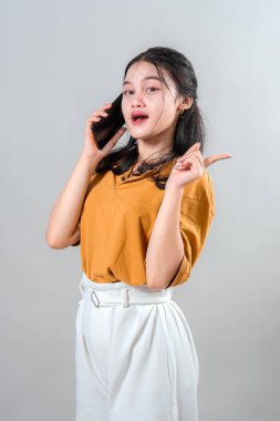 Genç Asyalı kadın telefonda konuşurken şaşırmış ve heyecanlı bir yüz ifadesi sergiliyor. Canlandırıcı jesti ve canlı görünümü onu iletişimle ilgili reklam içeriği için ideal kılıyor..