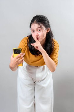 Genç Asyalı bir kadının esrarengiz bir ifadeyle şşşş hareketi yaptığı portresi. Parmağı dudaklarda ve doğrudan bakışlar gizemli ve ilgi çekici bir etki yaratır..