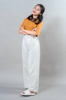 Genç Asyalı bir kadın samimi ve cana yakın bir ifadeyle gülümsüyor, kolları rahat bir şekilde kavuşturuluyor. Stüdyo portresi güven, sıcaklık ve pozitif kişilik aktarıyor..