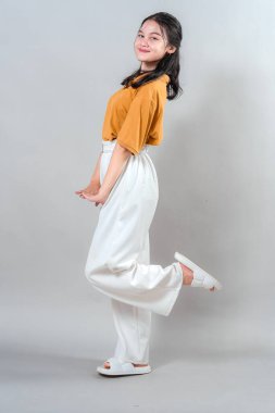 Genç Asyalı bir kadının neşeli ve çekici bir ifadeyle tatlı tatlı gülümsemesi, bir bacağını neşeli bir şekilde kaldırması. Olumlu, doğal ve neşeli bir stüdyo portresi..