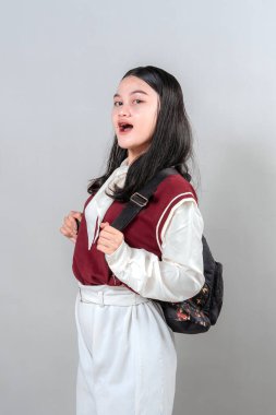 Sırt çantası takan gülümseyen genç bir kadın, kendine güvenen ve yumuşak bir ifadeyle yetinen. Modern görsel kampanyalarda eğitim, yaşam tarzı veya tanıtım reklamları için ideal.