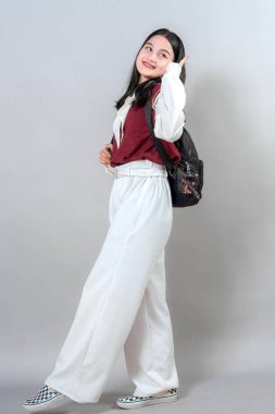 Neşeli bir ifadeyle gülümseyen genç bir kadın, yürürken yan yan bakıyor. Parlak yüzü ve kendine güveni onu gençlik hayatı reklamları için ideal kılıyor..