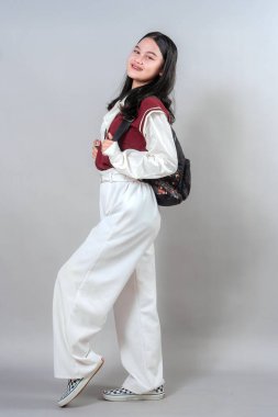 Sırt çantası takan gülümseyen genç bir kadın, kendine güvenen ve yumuşak bir ifadeyle yetinen. Modern görsel kampanyalarda eğitim, yaşam tarzı veya tanıtım reklamları için ideal.