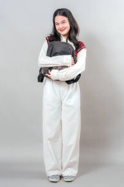 Sırt çantasını kucaklarken tatlı tatlı gülümseyen genç bir kadın samimiyet ve masumiyet gösteriyor. Onun nazik ifadesi ve doğal duruşu yaşam tarzı reklamları için davetkar bir ortam yaratıyor..