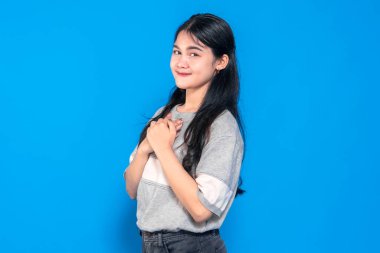 Uzun siyah saçlı genç Asyalı kadın ellerini göğsüne koyarken nazikçe gülümsüyor. Gri bir süveter giyiyor ve mavi bir arka plana karşı duruyor. Minnettarlığını ifade ediyor..