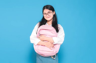 Beyaz üniformalı, mavi etekli, gözlüklü, pembe sırt çantasına sıcacık bir gülümsemeyle sarılan Endonezyalı bir liseli kız..