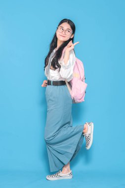 Beyaz üniformalı, mavi etekli, gözlüklü, pembe sırt çantalı, neşeli bir gülümsemeyle neşeli bir poz veren Endonezyalı bir liseli kız..