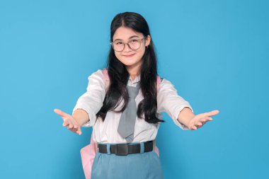 Beyaz üniformalı, mavi etekli, gözlüklü ve pembe sırt çantalı Endonezyalı bir liseli kız mavi bir arka plana karşı kollarını öne uzatarak yalvarıyor..