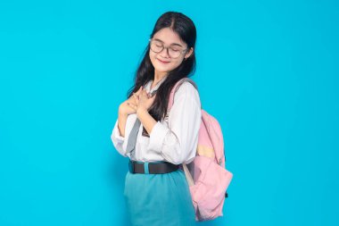 Endonezyalı bir lise öğrencisi, gözlüklü ve sırt çantalı, gözleri kapalı, elleri göğsünde gülümseyen parlak mavi bir geçmişe karşı şükranlarını sunuyor..