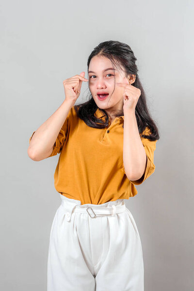 Young Asian woman makes a cute crying face while pointing to her eyes with both index fingers. Her playful and dramatic expression conveys mock sadness or teasing emotion.