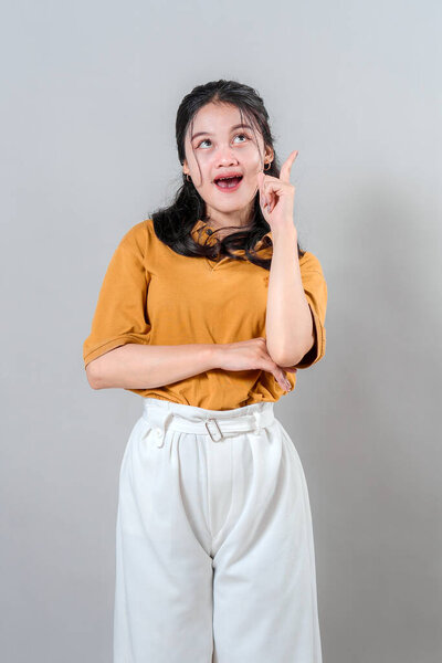 Excited young woman with surprised expression and open mouth, pointing upward with index finger as if getting a bright idea. Perfect for creative or inspirational themes.