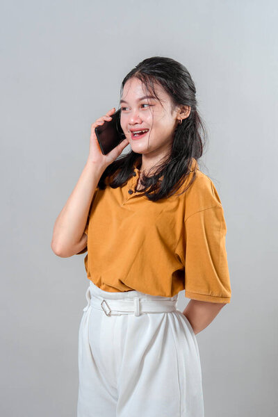 Happy young Asian woman laughing while talking on the phone. Her cheerful expression and genuine joy make this portrait ideal for advertising campaigns about connection and communication.