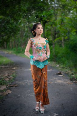 Renkli bir kebaya bürünmüş Endonezyalı güzel bir kadın çiçek işlemeli ve geleneksel batik etekli, zarif bir şekilde bir yolda duran, kültürel gurur, kadınlık ve zamansız zarafeti ifade eden.