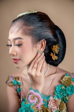 Renkli bir kebaya bürünmüş zarif bir Endonezyalı kadın. Karmaşık çiçek işlemeli, nazikçe küpesine dokunuyor. Güzelliğini, özgüvenini ve Endonezya kültürünün inceliklerini gösteriyor..