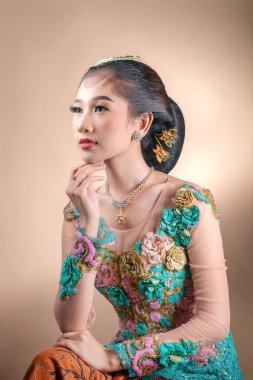 Zarif Endonezyalı bir kadın çiçek işlemeli renkli geleneksel bir kebaya giyer düşünceli bir ifadeyle zarif bir poz verir güzelliği, kültürü ve güveni temsil eder..