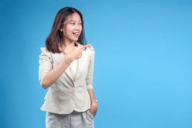 Endonezyalı kendine güvenen bir iş kadını resmi kıyafetler giyerken gülümseyip yan tarafa işaret ederek küresel kurumsal iletişim için olumlu ve profesyonel bir tutum sergiliyor..