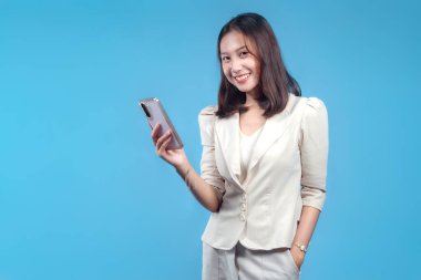 Endonezyalı kendine güvenen bir iş kadını elinde akıllı bir telefonla gülümseyip küresel kurumsal, iletişim ve dijital iş temalarına uyan modern ve profesyonel bir görünüm sunuyor..