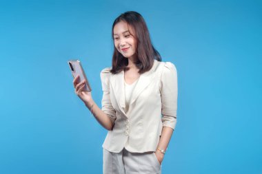 Akıllı telefonunu kontrol ederken gülümseyen kendine güvenen Endonezyalı bir iş kadını, temiz bir ortama karşı resmi giyinmiş, küresel iletişim temalarına uygun pozitif ve modern bir kurumsal konsept sunuyor..