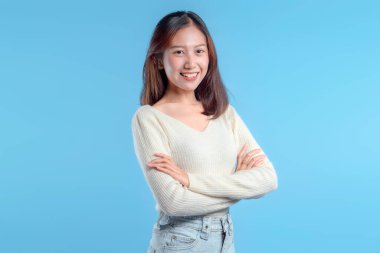 Gülümseyen Endonezyalı bir kadın, kollarını kavuşturmuş, açık renk bir süveter ve kot pantolon giyiyor, sıcaklığını, pozitifliğini ve modern profesyonel görünümünü ifade ediyor..