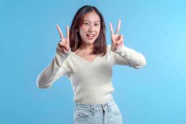 Endonezyalı bir kadın çok yönlü reklam kullanımı için temiz mavi bir arka plana karşı neşe, neşe ve neşe ve enerji dolu pozitifliği ifade eden, açık bir çifte barış işareti yapmak için iki elini kaldırırken geniş bir gülümseme içinde..