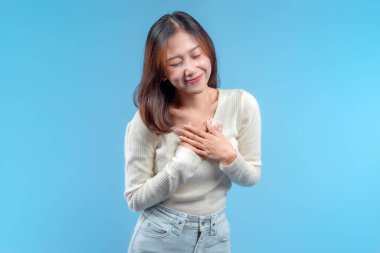 Ellerini göğsüne koyan, krem rengi bir kazak ve kot giyen, sıcak ve minnettar bir yüz ifadesiyle Endonezyalı bir kadın, olumlu ve dostane bir anda yakalandı..