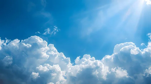 Mavi gökyüzünün altında güneş ışınlarıyla dolu canlı kümülüs bulutları. Aralık 'ta iklim görselleri, doğa kampanyaları ve Uluslararası Dağ Günü için ideal.